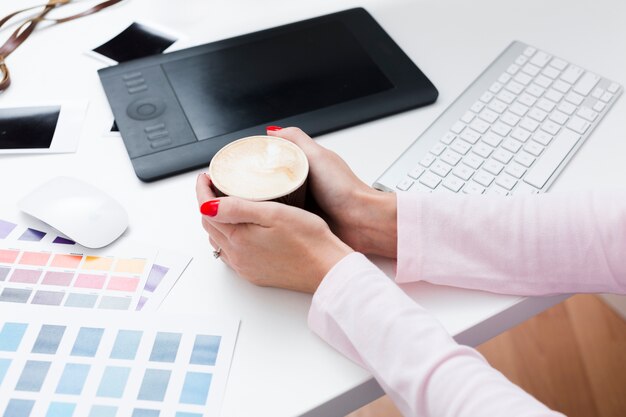 High angle of cup of coffee held by woman on desk