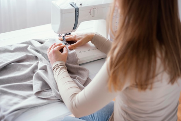 High angle of female tailor with sewing machine and fabric