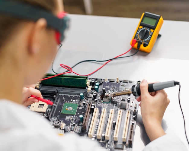 Free Photo high angle of female technician with soldering iron and electronics motherboard