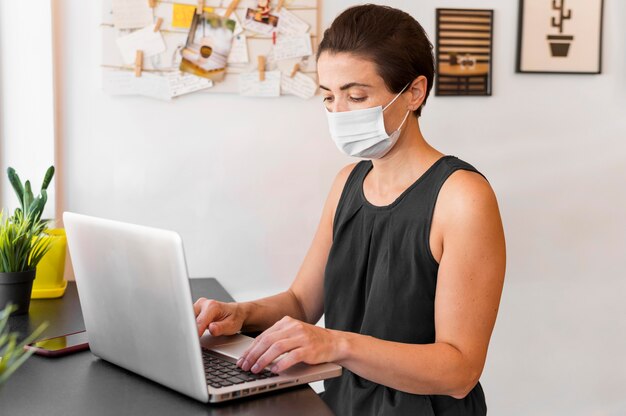 High angle female with mask working on laptop