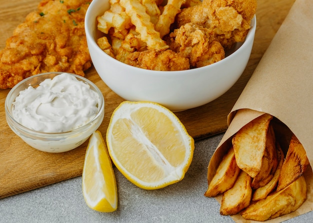 Free photo high angle of fish and chips in bowl and paper wrap with lemon