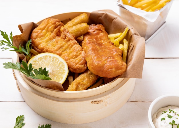 High angle of fish and chips in bowl with lemon