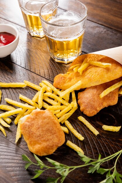 High angle of fish and chips in paper cone with beer