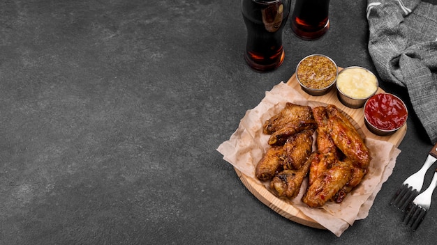 High angle of fried chicken wings with variety of sauces and fizzy drinks