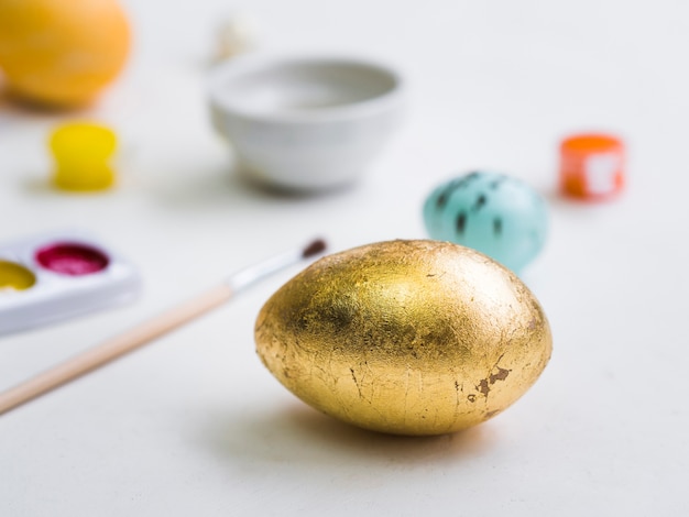 High angle of golden easter egg with defocused palette and brush