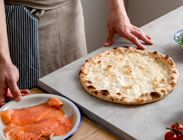 Free photo high angle man standing near baked pizza dough and smoked salmon slices