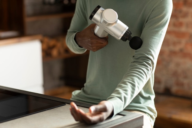 Free photo high angle man using massage gun for arm