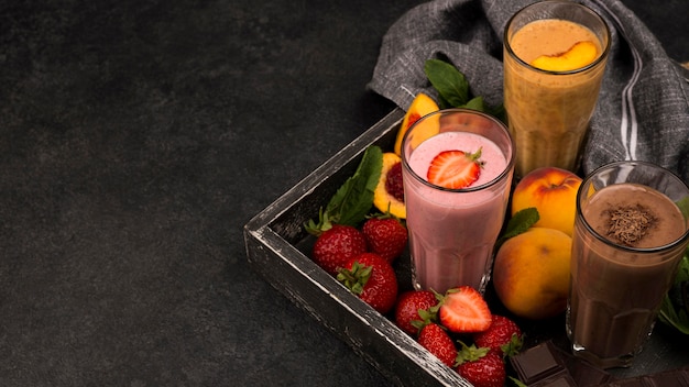 High angle of milkshake glasses on tray with chocolate and fruits