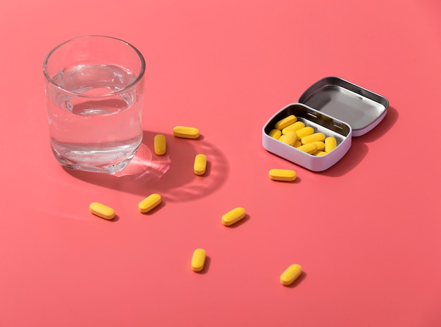 High angle of pills in metal container with glass of water