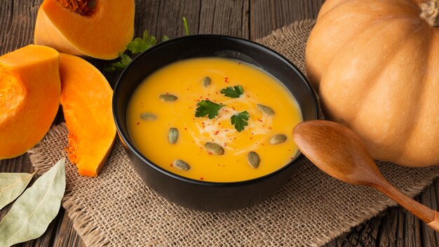 High angle pumpkin soup in bowl with pumpkin and wooden spoon