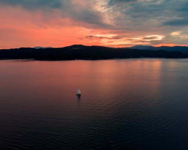 Free Photo high angle shot of the beautiful sea with a single boat sailing at sunset