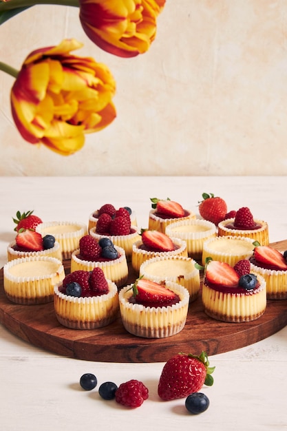 Free photo high angle shot of cheese cupcakes with fruit jelly and fruits on a wooden plate