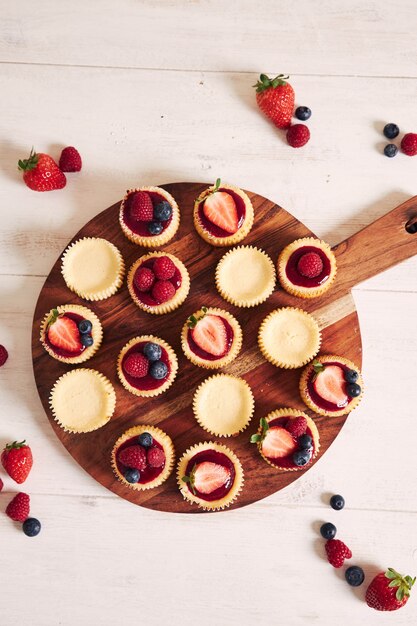 High angle shot of cheese cupcakes with fruit jelly and fruits on a wooden plate