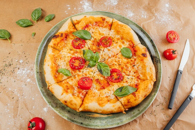 High angle shot of a delicious pizza with sliced tomato and basil leaves