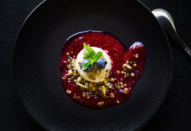 High angle shot of a delicious red dessert with white cream, berries and nuts in a black bowl