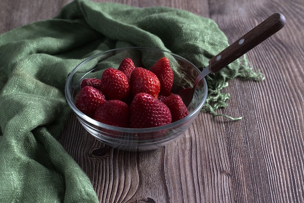 High angle shot of fresh strawberries and a green textile in a glass bowl on a wooden surface