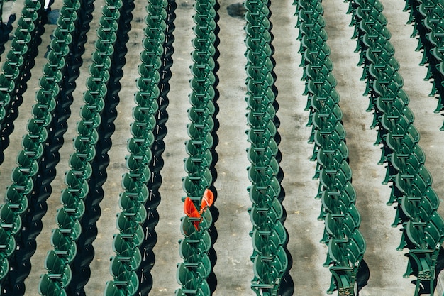 Free photo high angle shot of green plastic chair rows with only one orange chair in the middle