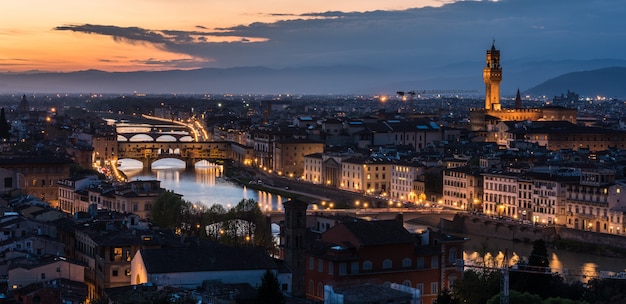 High angle shot of a lot of buildings with lights and a bridge in the evening