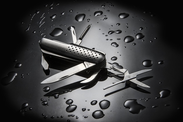 Free photo high angle shot of metal multi-purpose knife with water droplets isolated on black surface