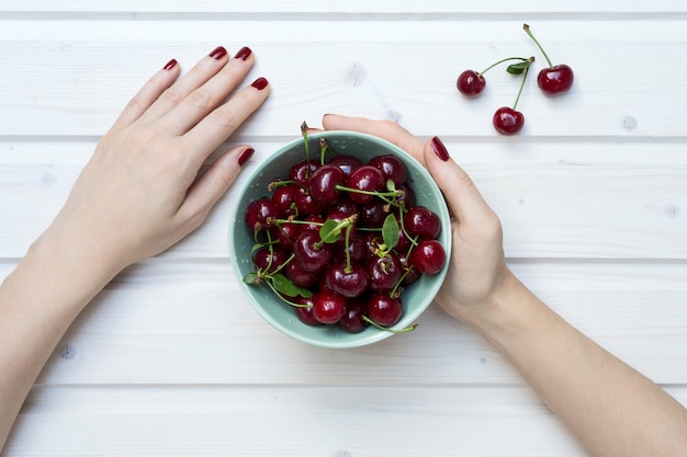 Free photo high angle shot of a person holding a green bowl of cherries on a white wooden surface