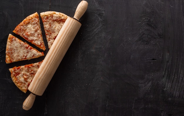 High angle shot of pizza pieces and a wooden roller on a wooden