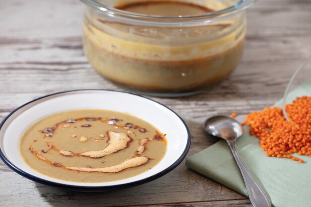 High angle shot of a pot and a bowl of soup and a spoon on a wooden surface