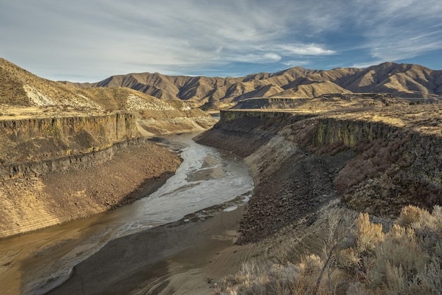 Free photo high angle shot of a river in the middle of cliffs with mountains in the distance under a blue sky