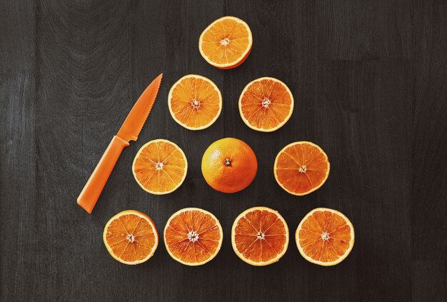 High angle shot of sliced oranges in a triangle shape beside an orange knife on a black surface