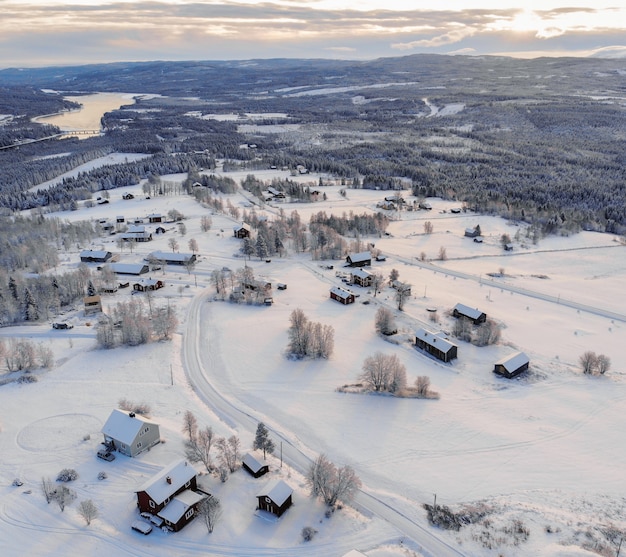 High angle shot of a town covered in the snow surrounded by forests and a lake under a cloudy sky