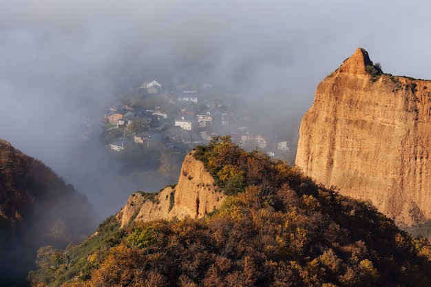 Free photo high angle shot of a tree-covered mountain with a village captured in the fog