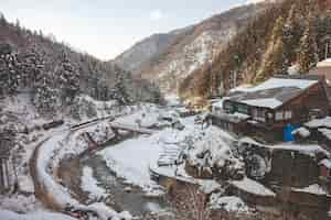 Free photo high angle shot of a wooden house surrounded by forested mountain covered in snow in winter