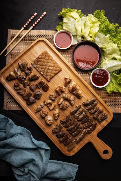 Free photo high angle shot of a wooden tray of fried meat, potatoes, vegetables, and sauce on a black table