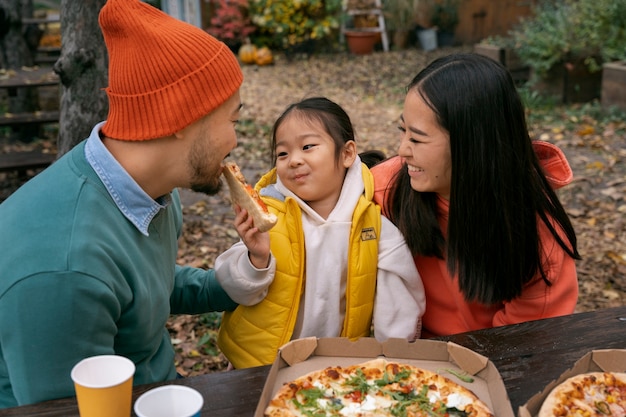 Free photo high angle smiley family with pizza outdoors