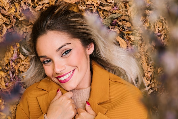 Free Photo high angle view of beautiful woman lying on dry leaves looking at camera