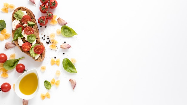 Free photo high angle view of bruschetta with farfalle raw pasta; garlic clove; tomato; oil; basil leaf against isolated on white background