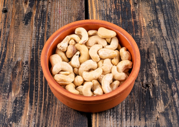 Free photo high angle view cashews in pottery on wooden table.