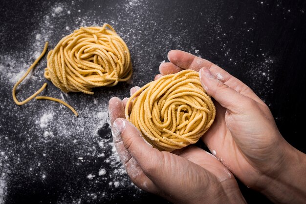 High angle view of chef holding spaghetti pasta nest over kitchen worktop