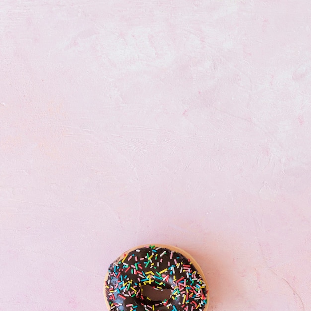 High angle view of chocolate donut with sprinkles at the bottom of pink background