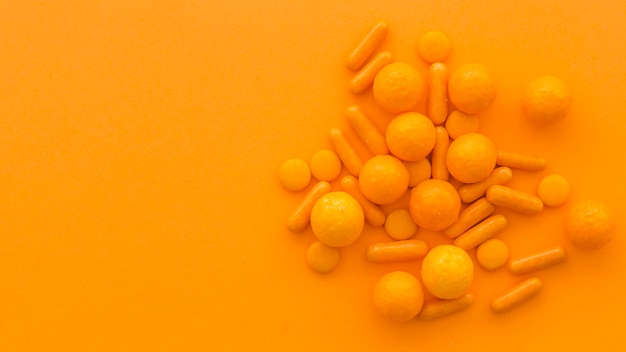 Free Photo high angle view of circular and capsule shape candies on orange background