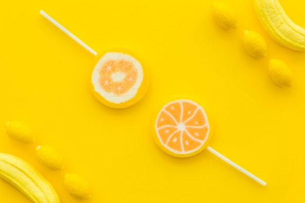 High angle view of citrus lollipops; banana and lemon candies on yellow background