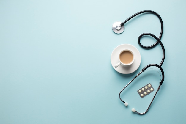 Free photo high angle view of coffee cup; stethoscope and medicine in blister pack over blue backdrop