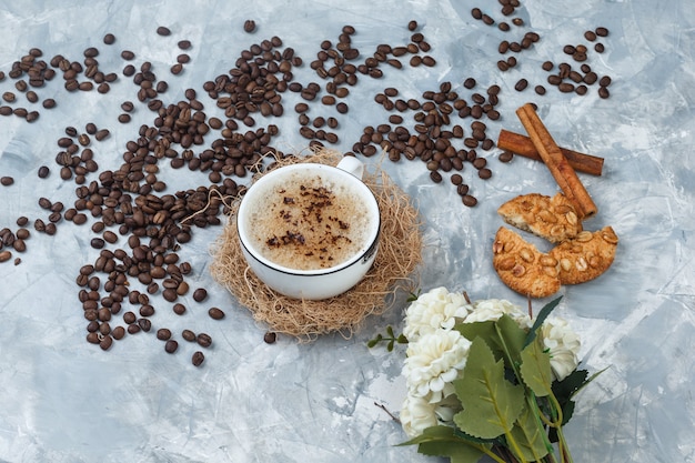 Free photo high angle view coffee in cup with cookies, coffee beans, flowers, cinnamon sticks on grey plaster background. horizontal