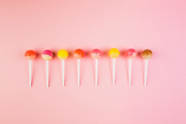 High angle view of colorful lollipops in a row on pink surface