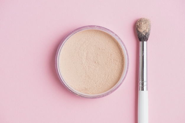 High angle view of compact powder and brush on pink backdrop