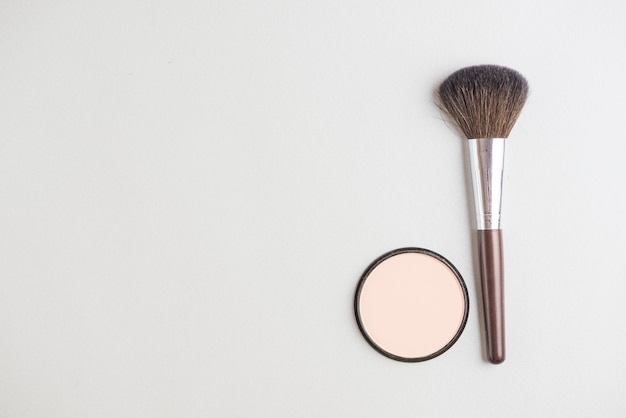 High angle view of cosmetic powder and brush on white backdrop