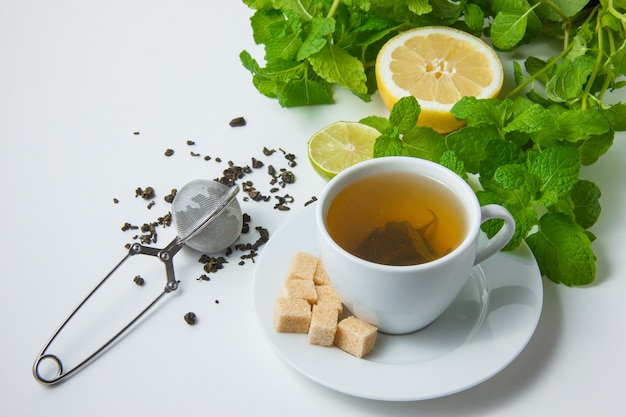 High angle view a cup of tea with lemon, sugar, mint leaves on white surface. horizontal