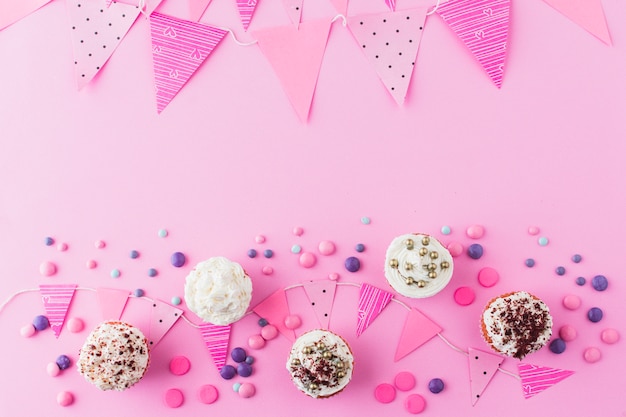 Free photo high angle view of cupcakes; candies and bunting on pink background