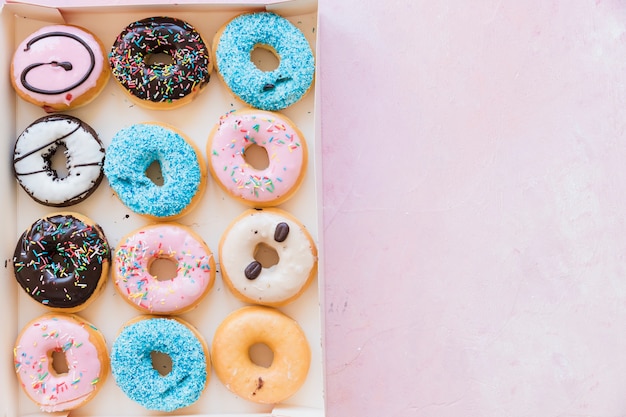 Free photo high angle view of delicious donuts in box on pink surface