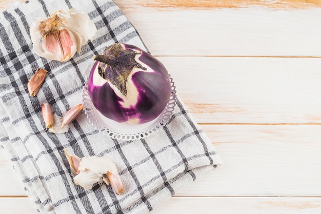 High angle view of eggplant and garlic cloves on chequered pattern cloth over wooden plank