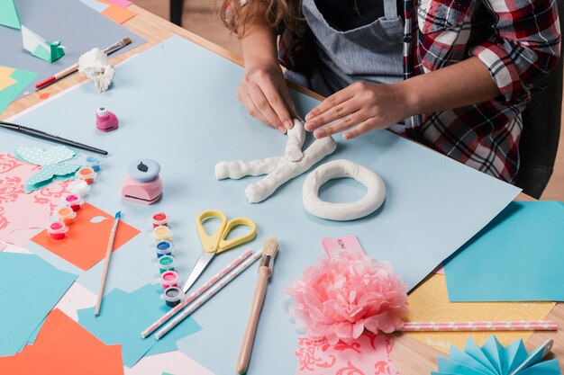 High angle view of female artist making letter with white clay over desk